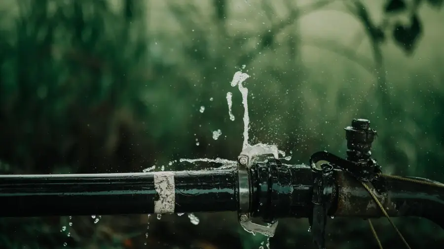 Black water pipe with a failed coupling spraying and dripping water against a blurred green background