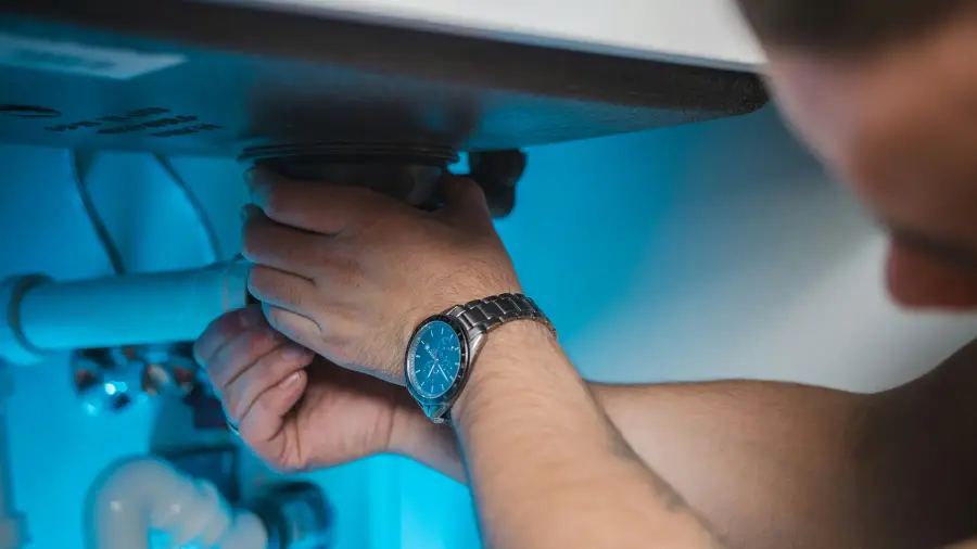 Plumber's hands working on the drain assembly beneath a kitchen sink